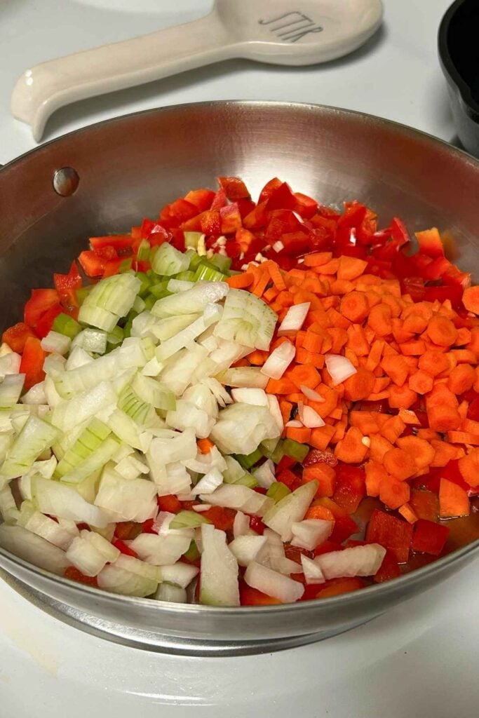 Chopped celery, onion, carrots, and red bell pepper in a stainless steel skillet.