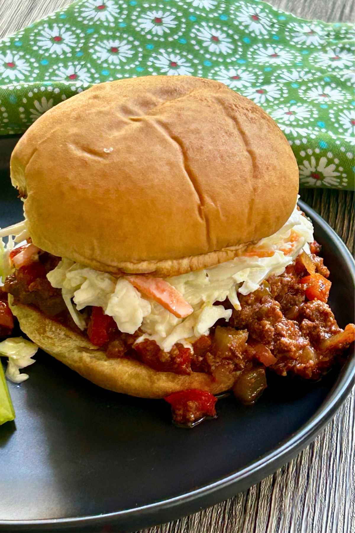 An image of sloppy joes without ketchup topped with a scoop of coleslaw in a bun on a black plate.