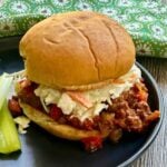 A sloppy joe sandwich topped with a scoop of coleslaw on a black plate.