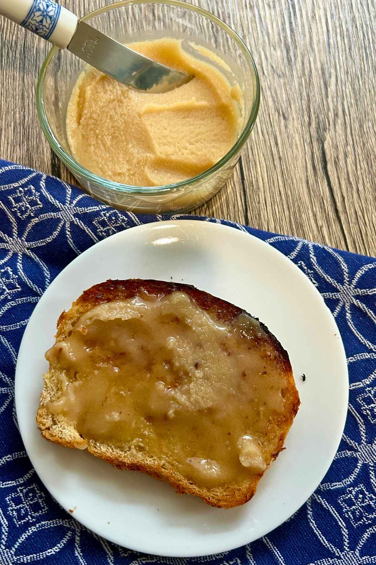 A slice of toasted bread spread with whipped maple butter on a small white plate next to a bowl of maple butter.