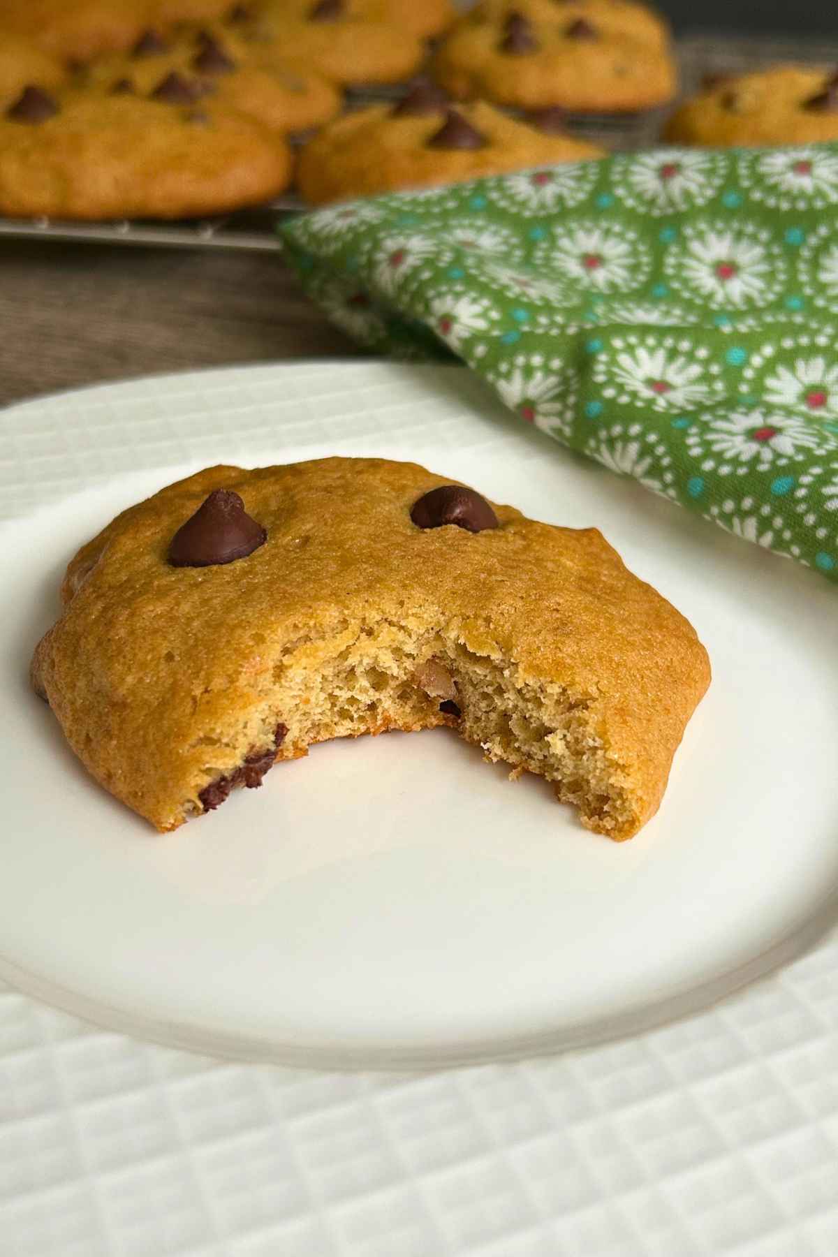 One soft cookie on a white plate with a bite taken out of the cookie.