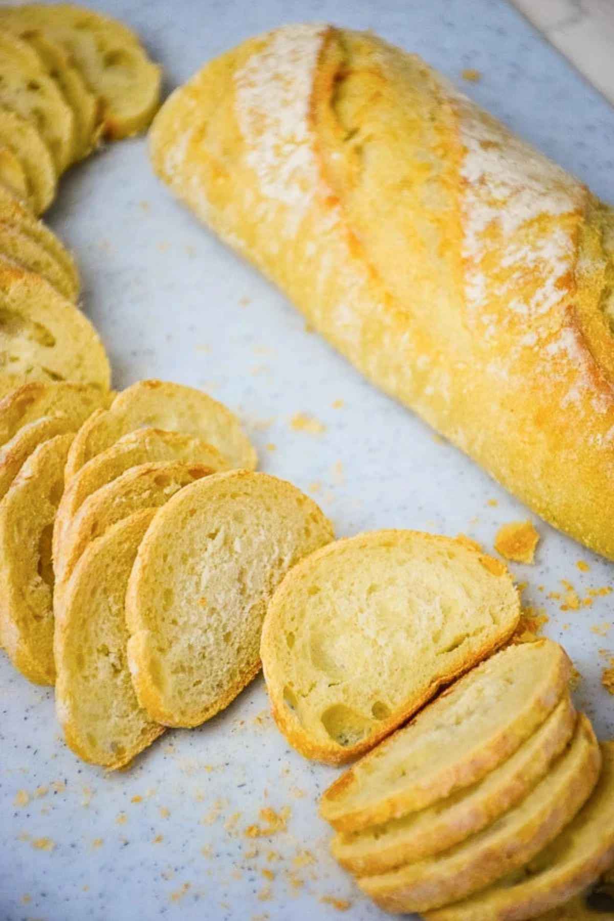 A baguette on a cutting board with thin slices cut from it.