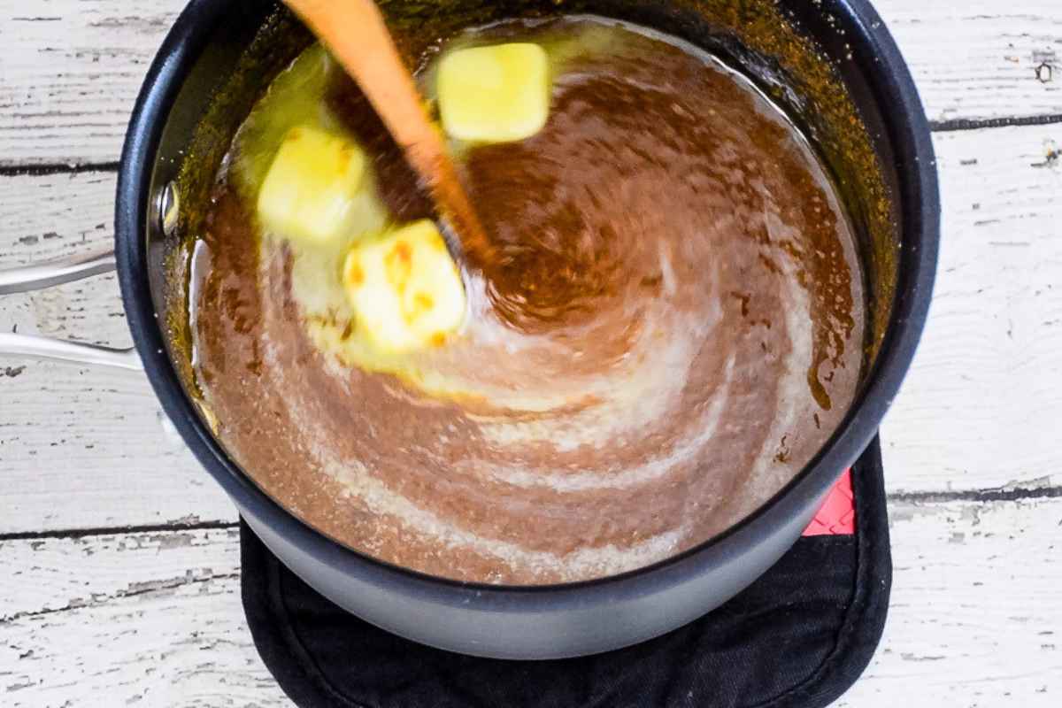 Cubes of butter being stirred into a hot fudge mixture.