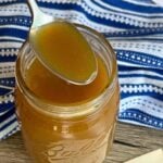 A silver spoon holding rich, golden butterscotch sauce over an open Ball Mason jar with a vintage handwritten recipe card reading "Butterscotch Sauce."