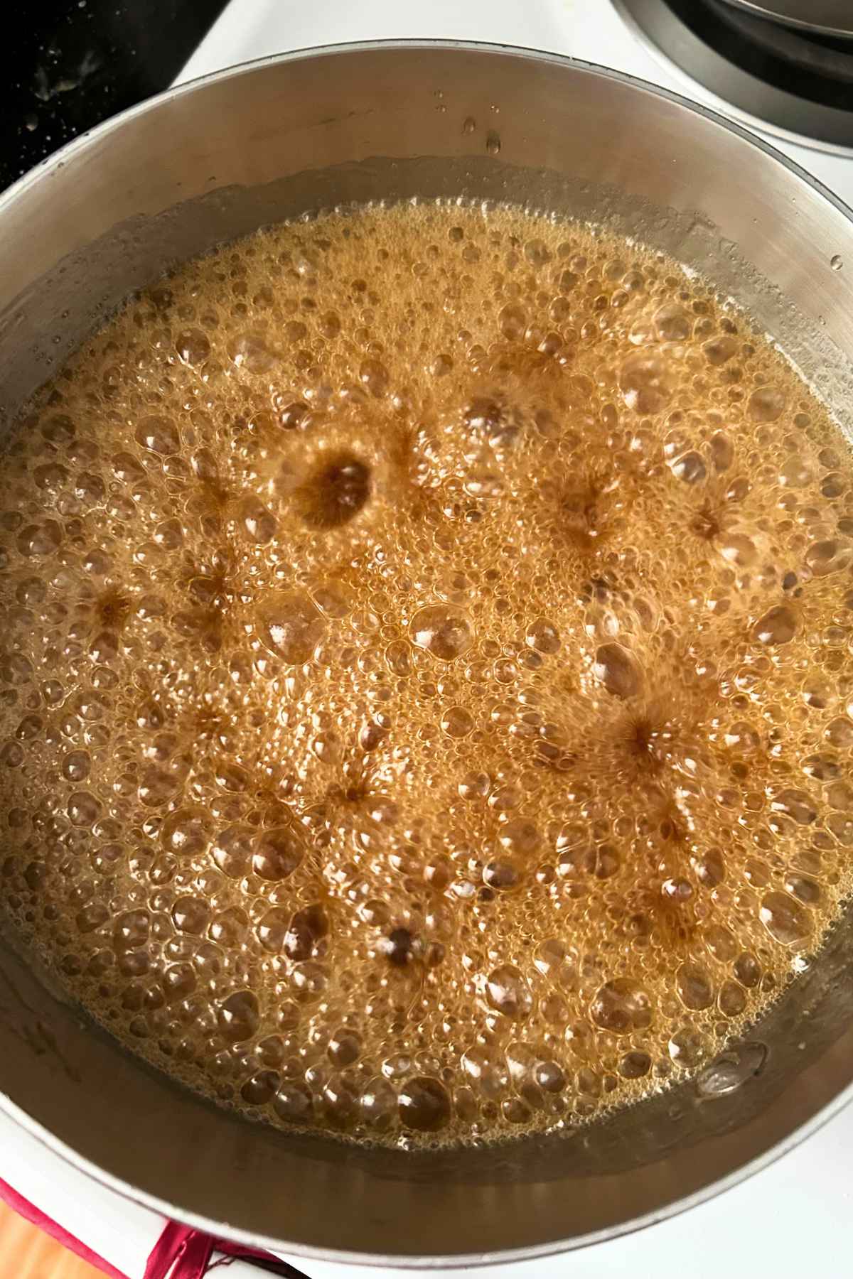 Golden sauce actively boiling and bubbling in a stainless steal saucepan on the stovetop.