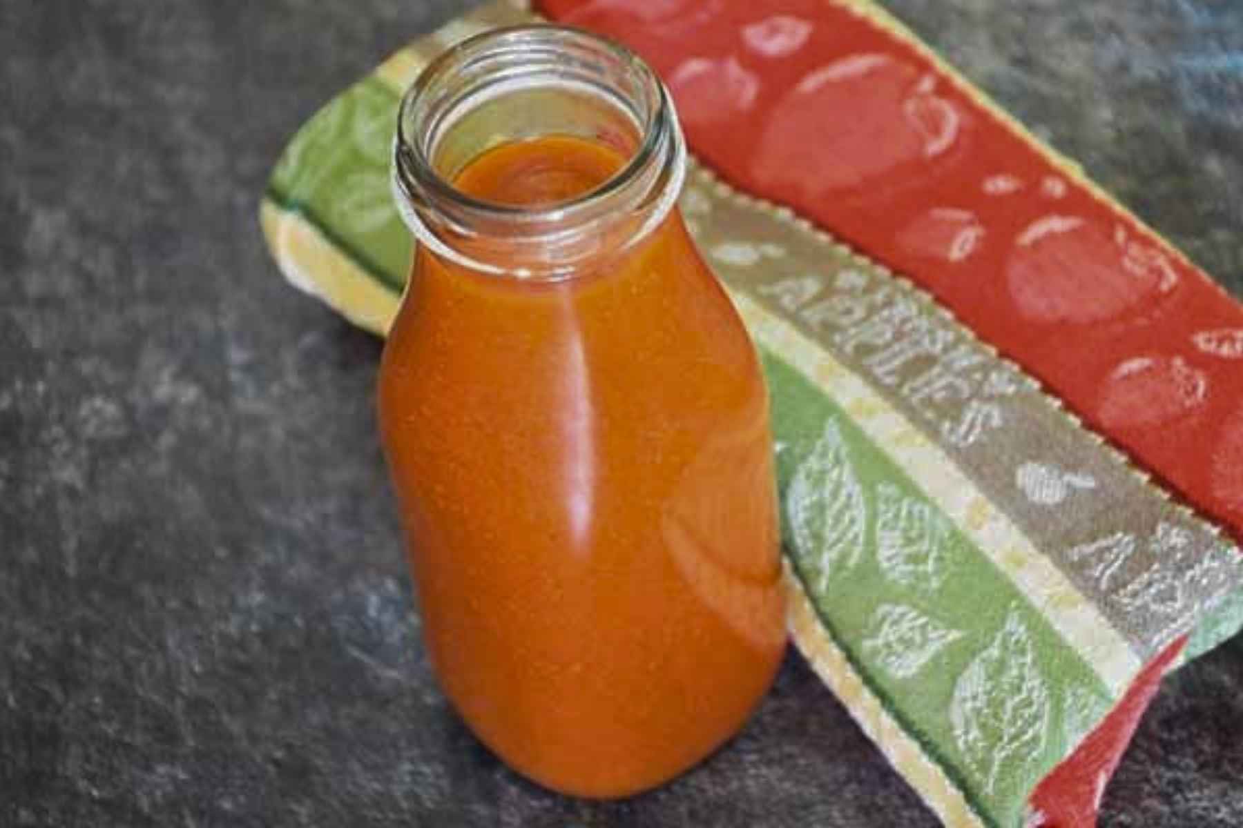 Glass jar filled with smooth, orange-red sauce against a blurred dark background.
