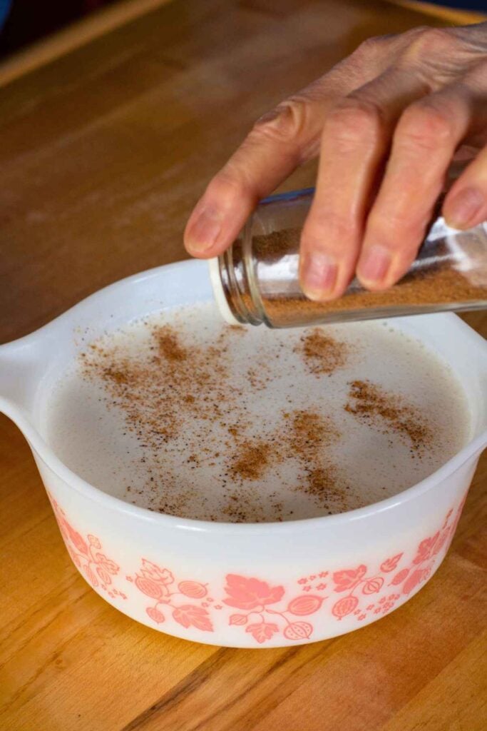 Sprinkling cinnamon on unbaked rice pudding in dish before placing in oven.