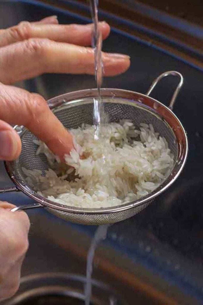 Rinsing long grain rice in a sieve under a water faucet.