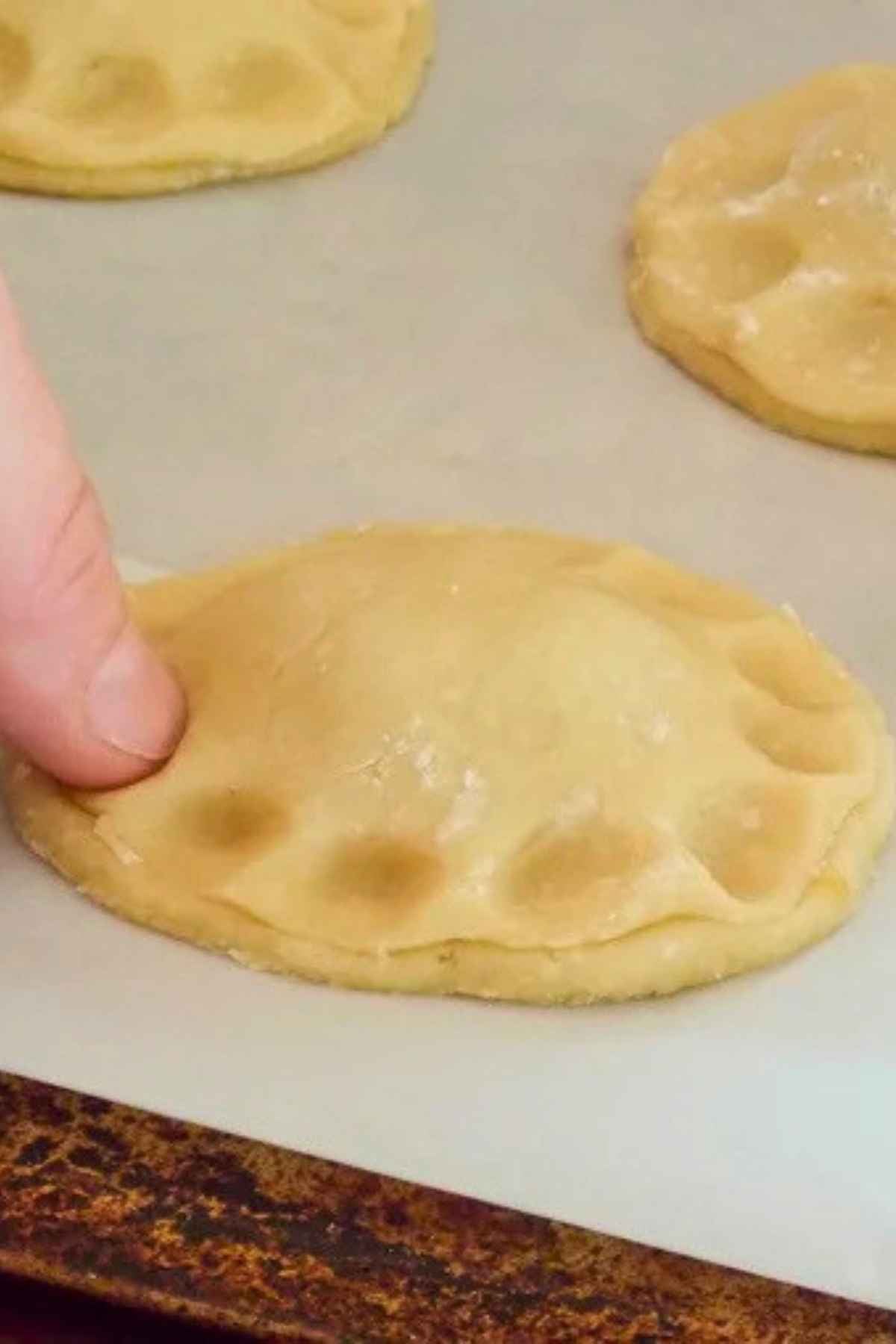 A finger pressing down along the edge of a round dough pocket to seal it closed.