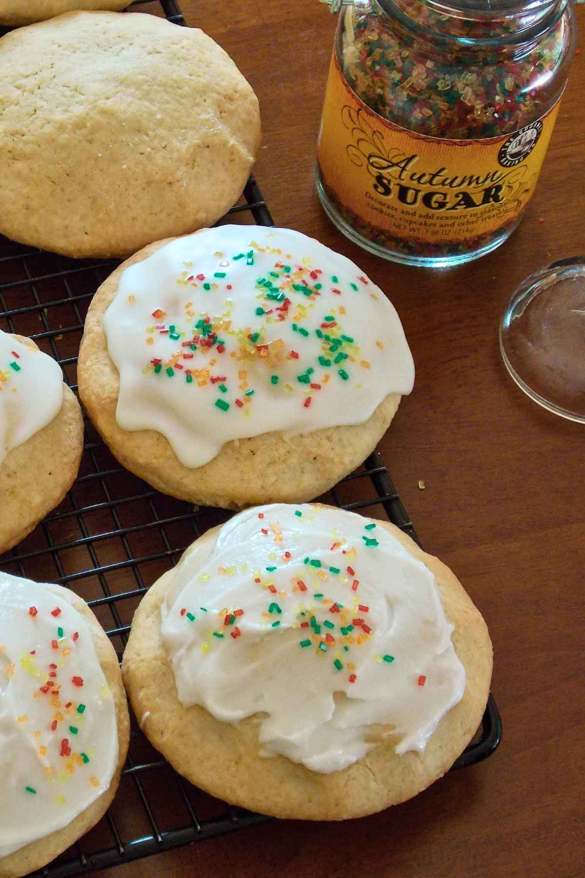 Top-down view of frosted raisin filled cookies with colorful sprinkles cooling on a wire rack.