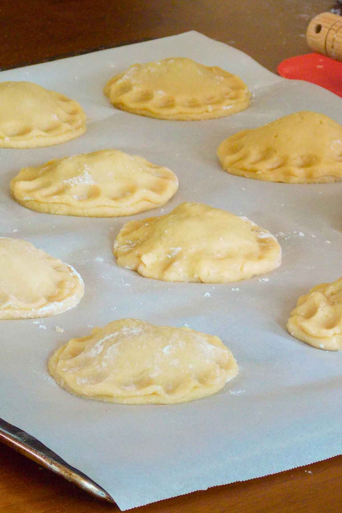 Multiple unbaked round dough pockets with sealed, crimped edges resting on parchment paper atop a baking sheet before being baked.