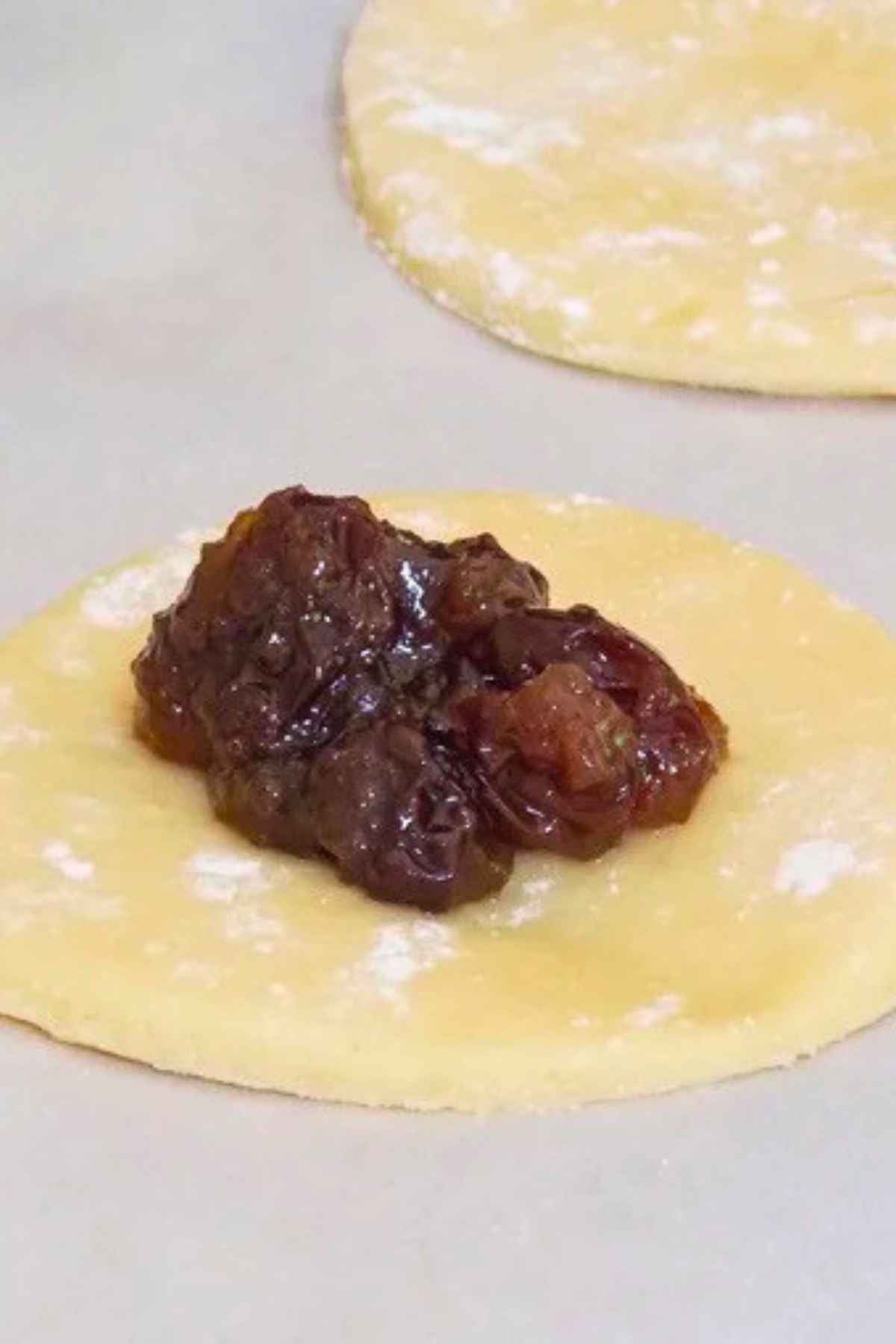 A scoop of thick raisin filling placed in the center of a round circle of unbaked cookie dough.