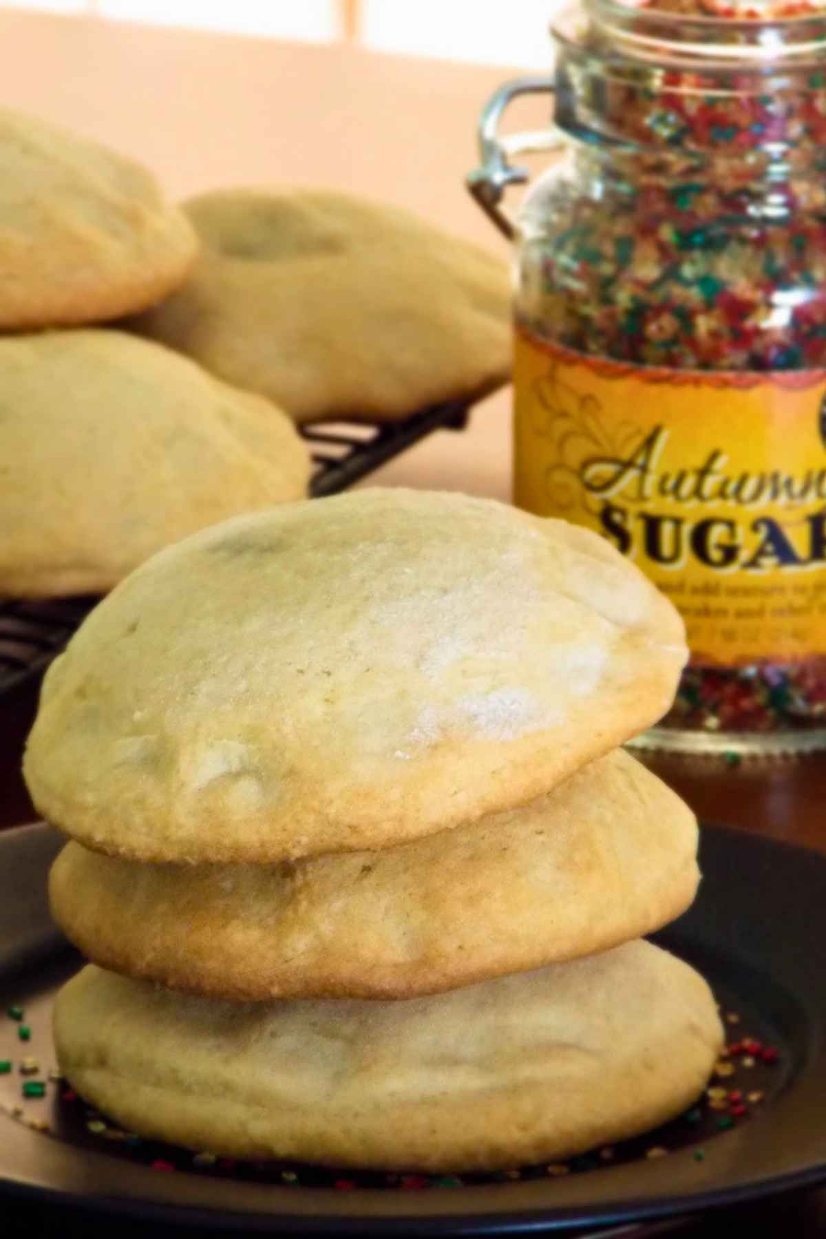 A stack of three round soft raisin filled cookies on a dark plate beside a glass container labeled "Autumn Sugar" against a warm background.