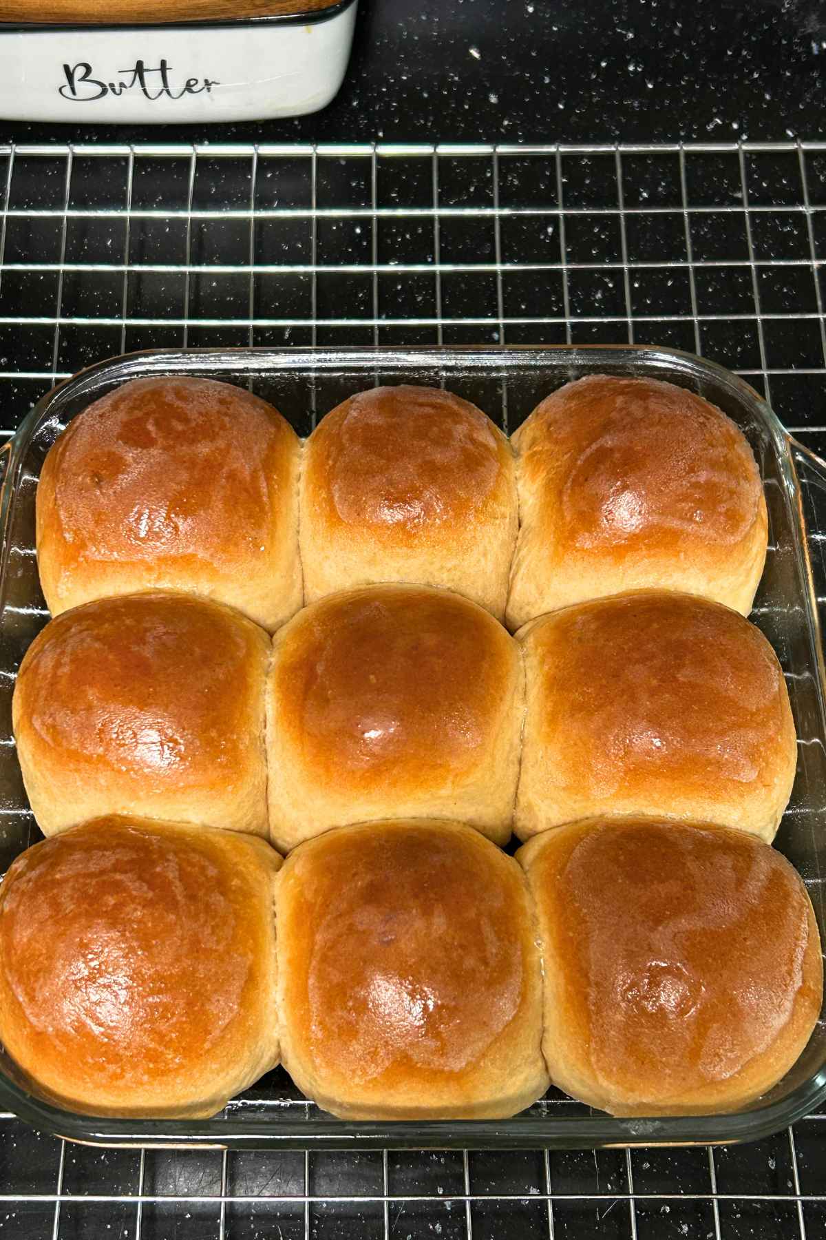 Overhead image of a square glass baking dish with nine golden brown baked dinner rolls that have been brushed with butter when hot.