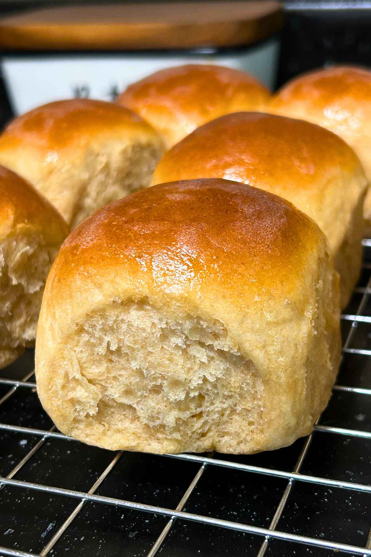 Close-up of a freshly baked golden-brown whole wheat dinner roll on a wire cooling rack.