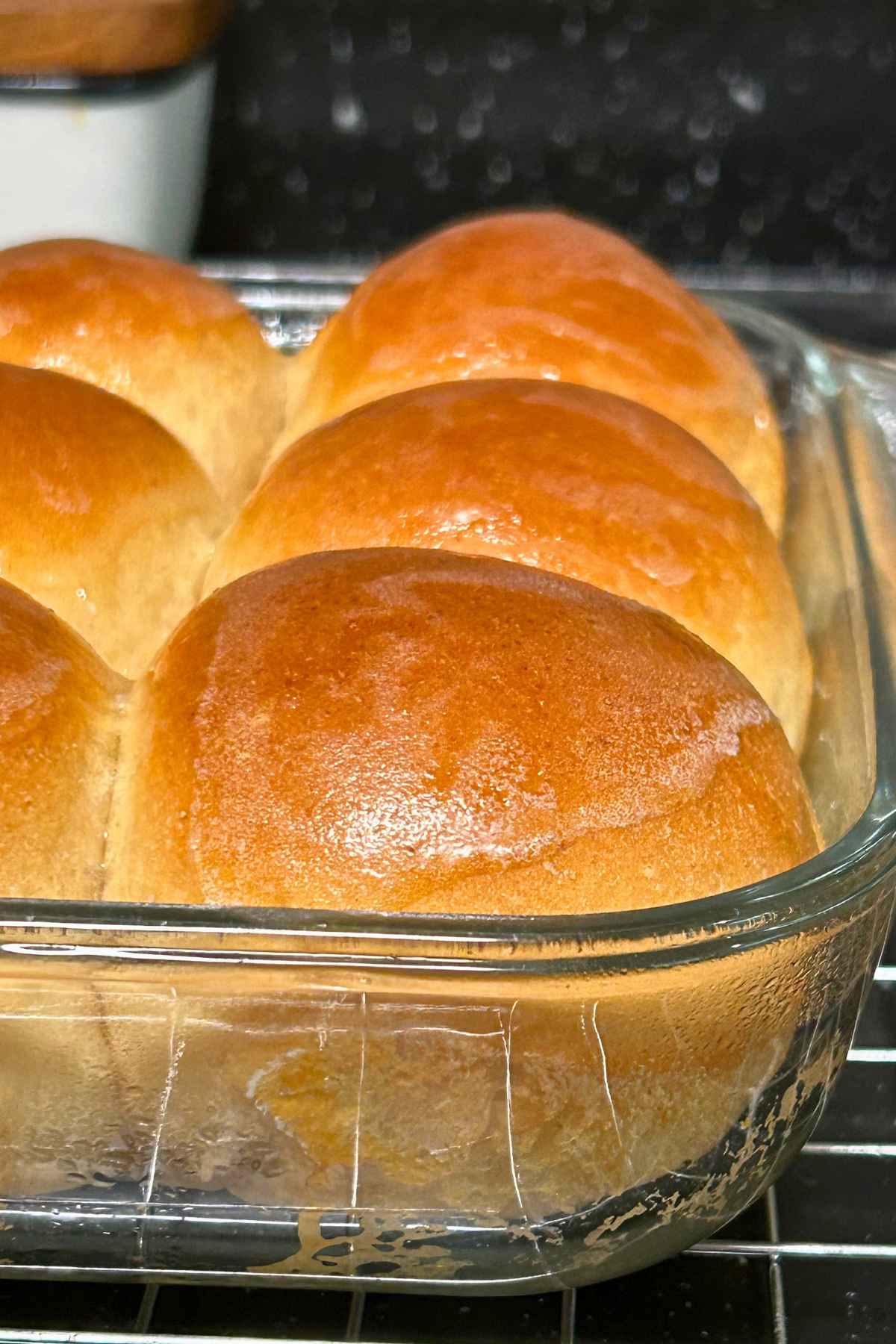 Golden brown wheat dinner rolls freshly baked in a clear glass dish.
