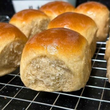 Close-up of a freshly baked golden-brown whole wheat dinner roll on a wire cooling rack.