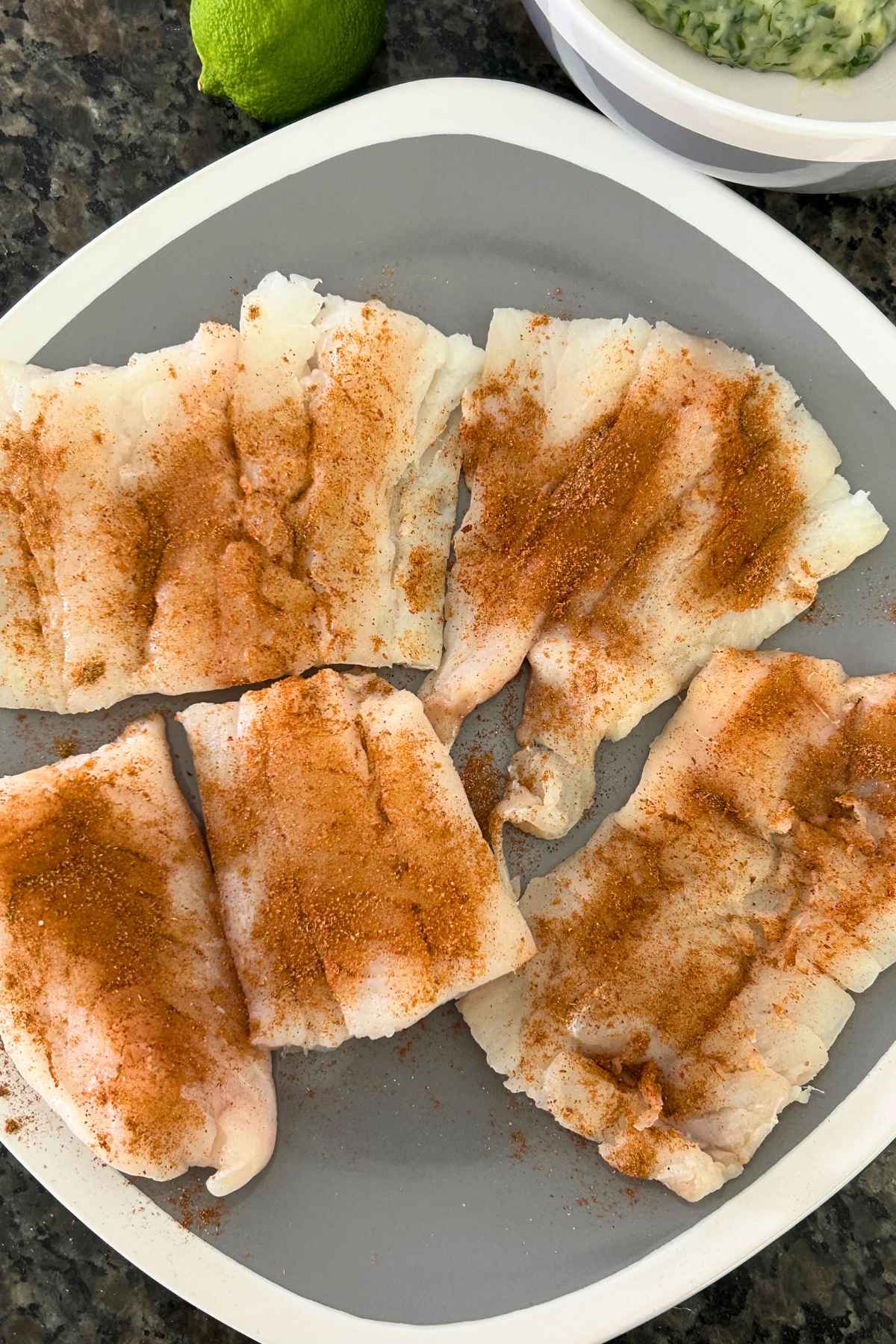 Raw fish fillets on a gray plate sprinkled with seasoning.