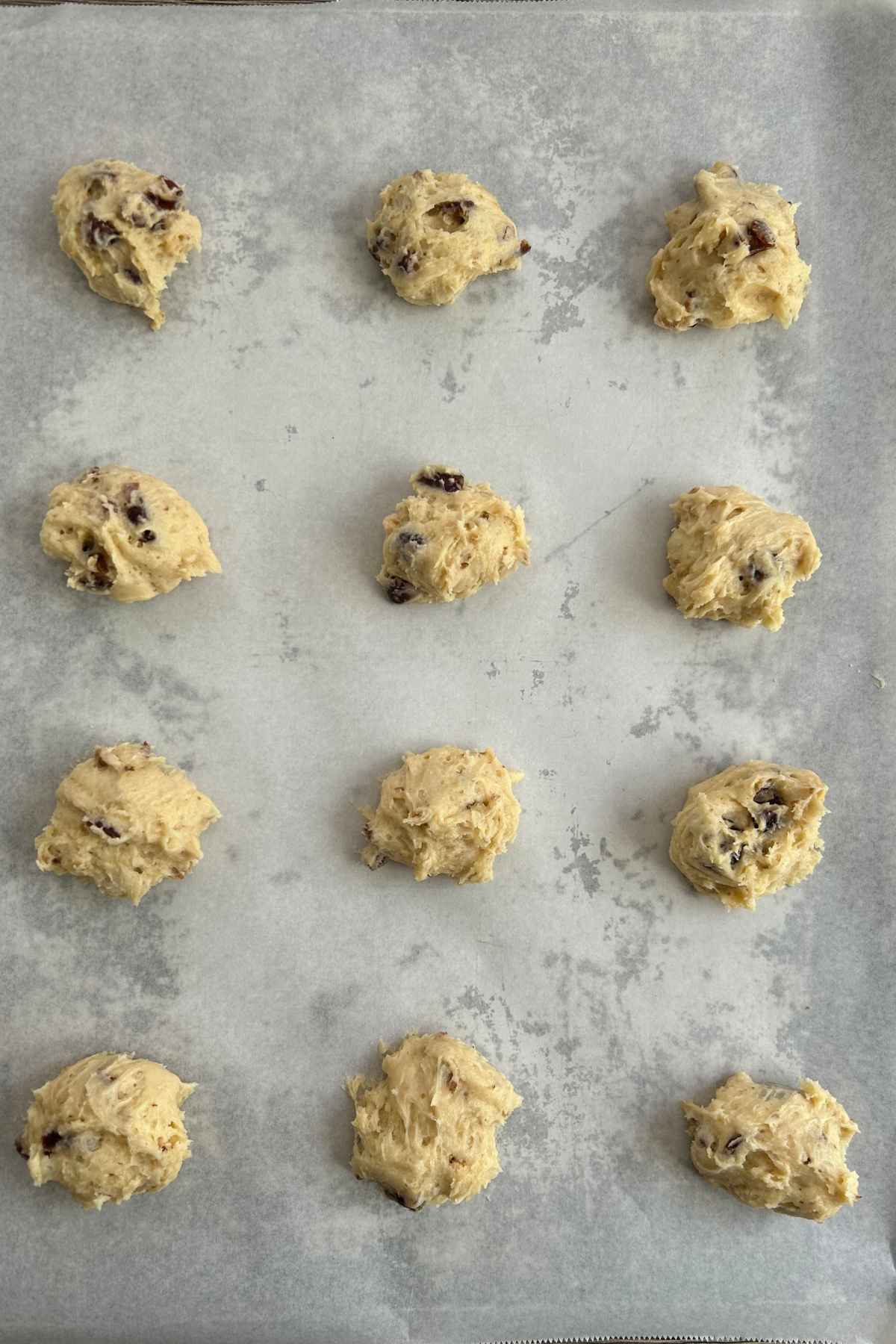 A dozen cookie dough balls on a parchment lined baking sheet.