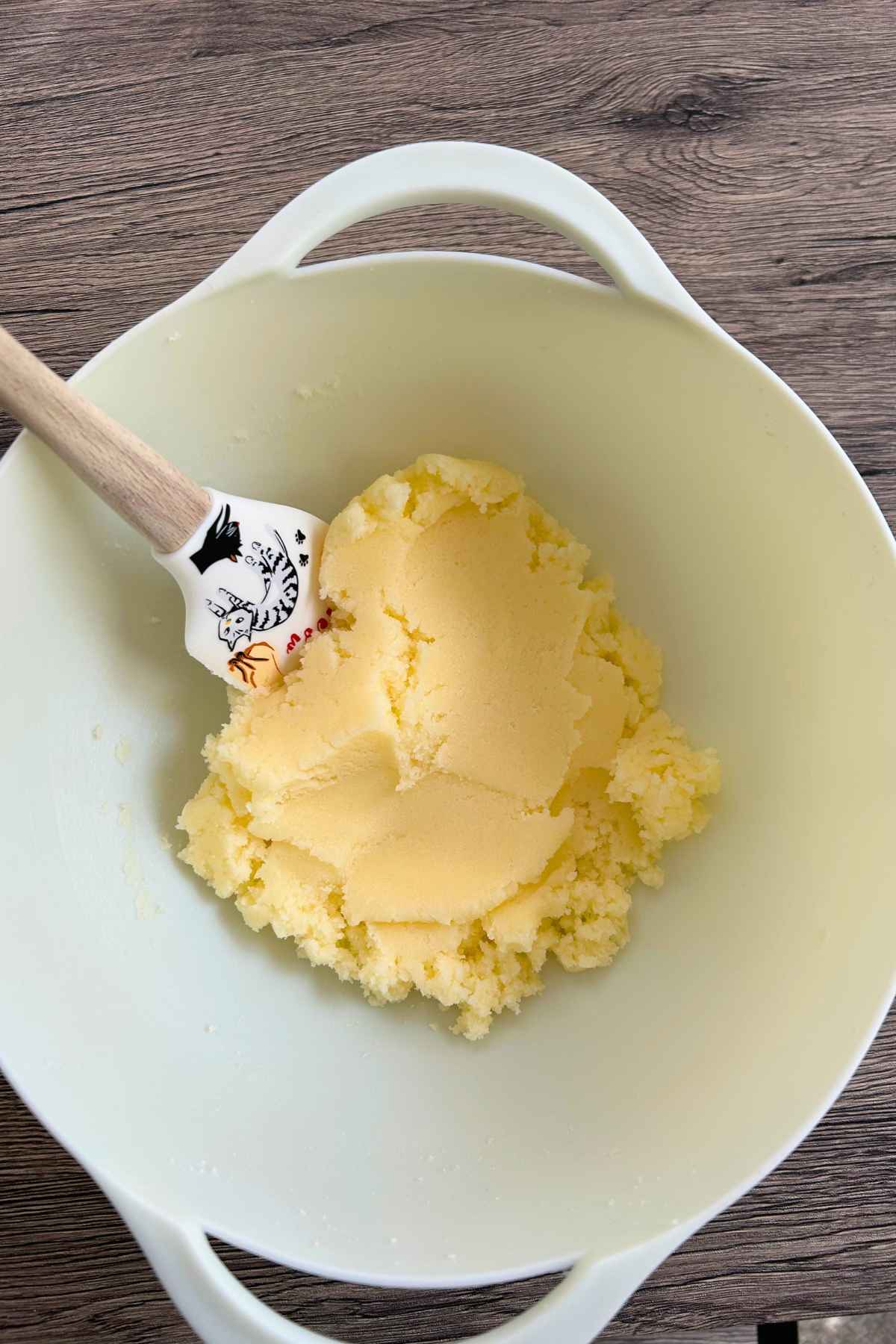 Creamed butter and sugar in a white bowl with a rubber scraper.