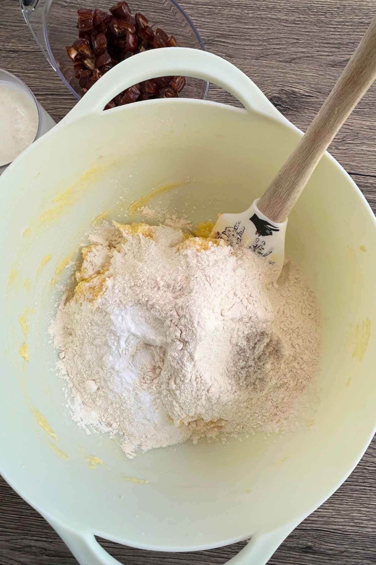 Dough in a white bowl topped with flour, baking powder, baking soda, and salt.