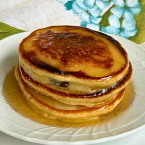 Upcloase shot of a stack of pancakes with syrup over top.