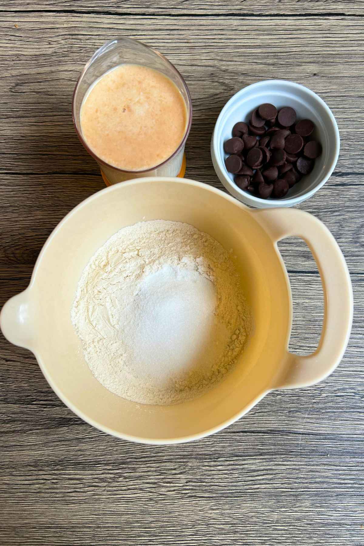 Dry ingredients in a mixing bowl, wet ingredients in a measuring cup and a white bowl of chocolate chips.