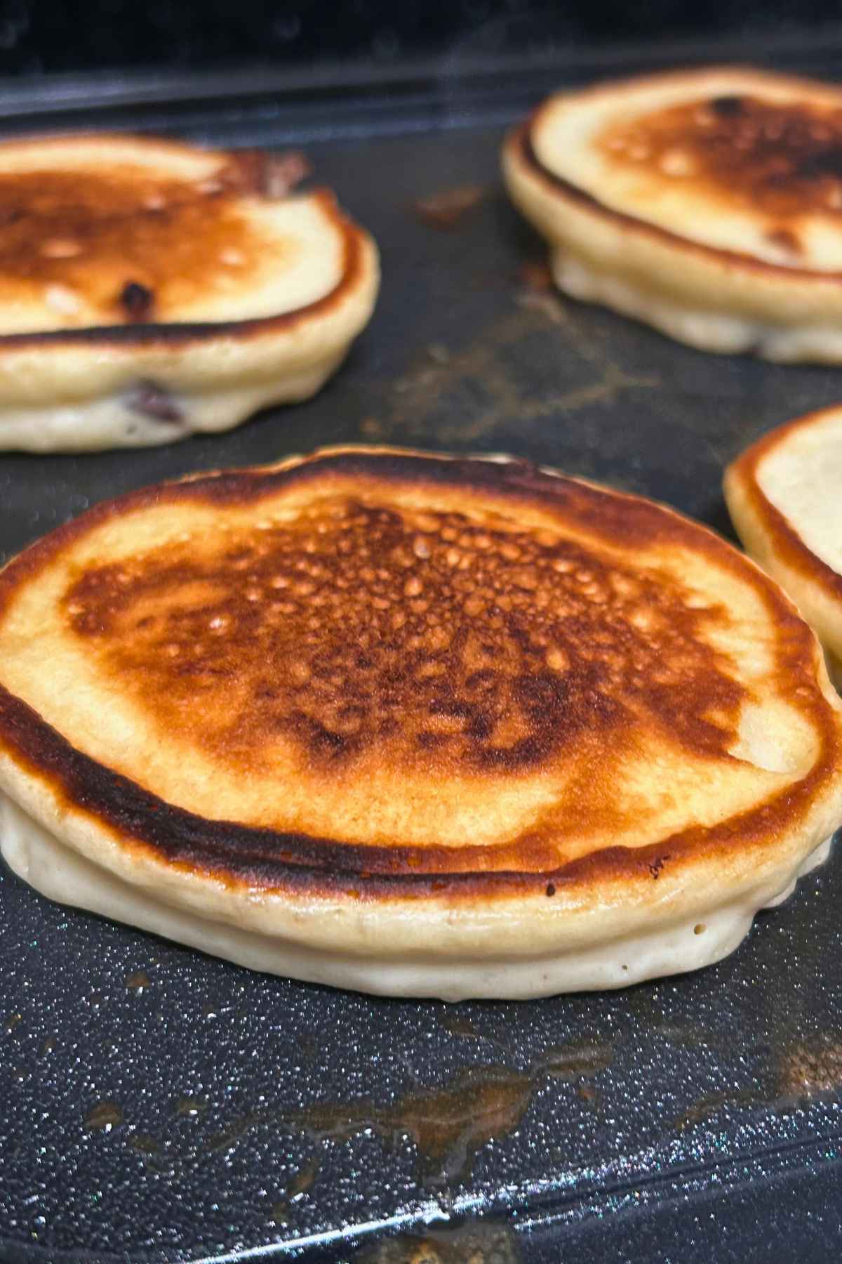 Close-up image of pancakes cooking on a griddle.