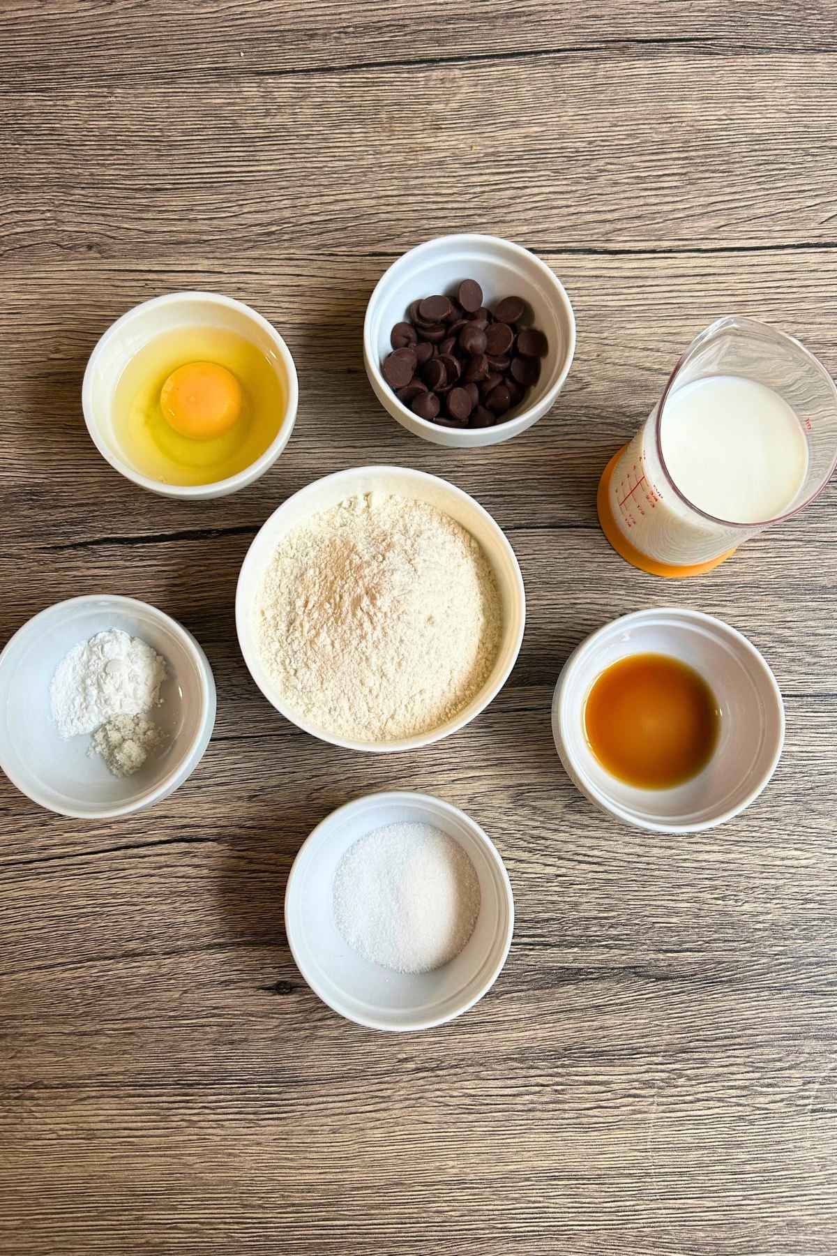Ingredients for Pancakes for two in white prep bowls: flour, sugar, baking powder, salt, vanilla, egg, milk, and chocolate chips.