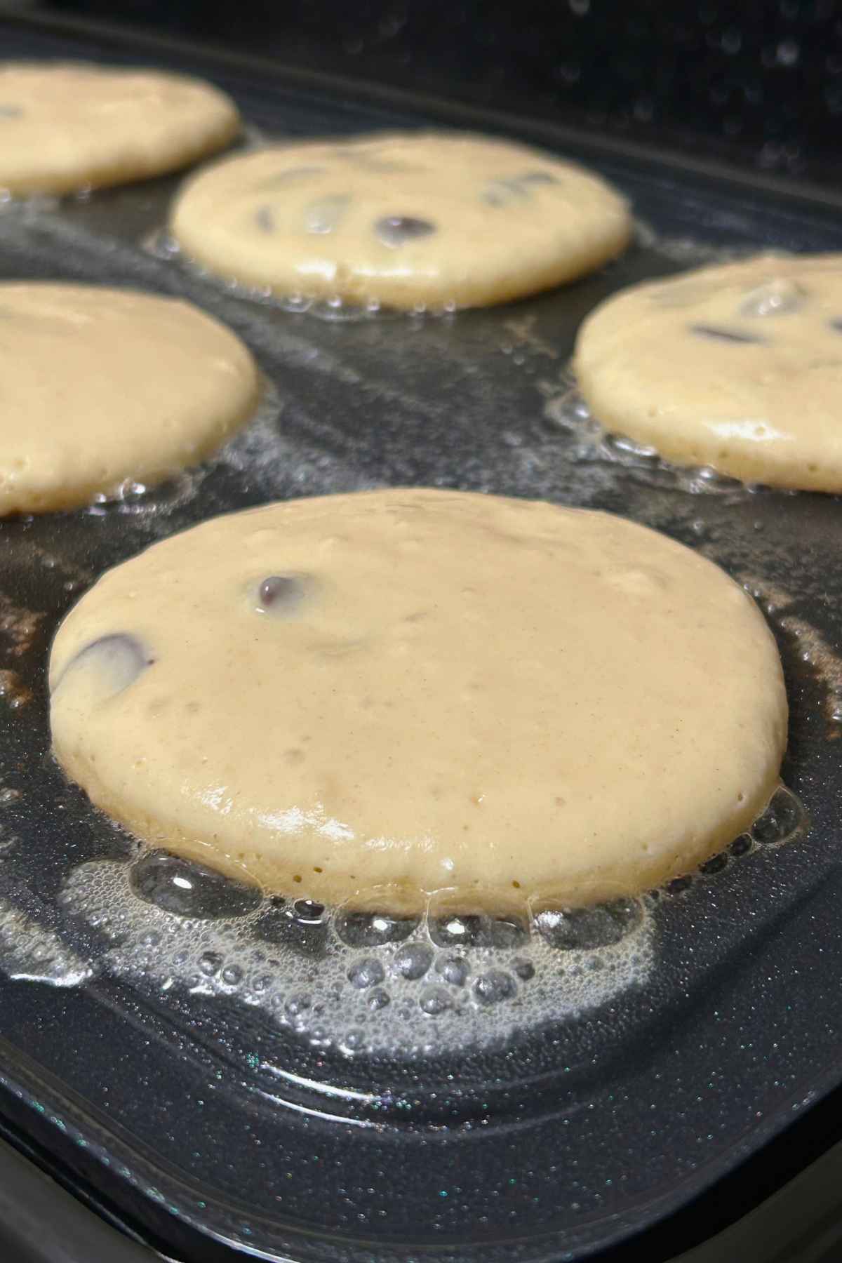 Pancake batter in circles on a bubbly buttered griddle.