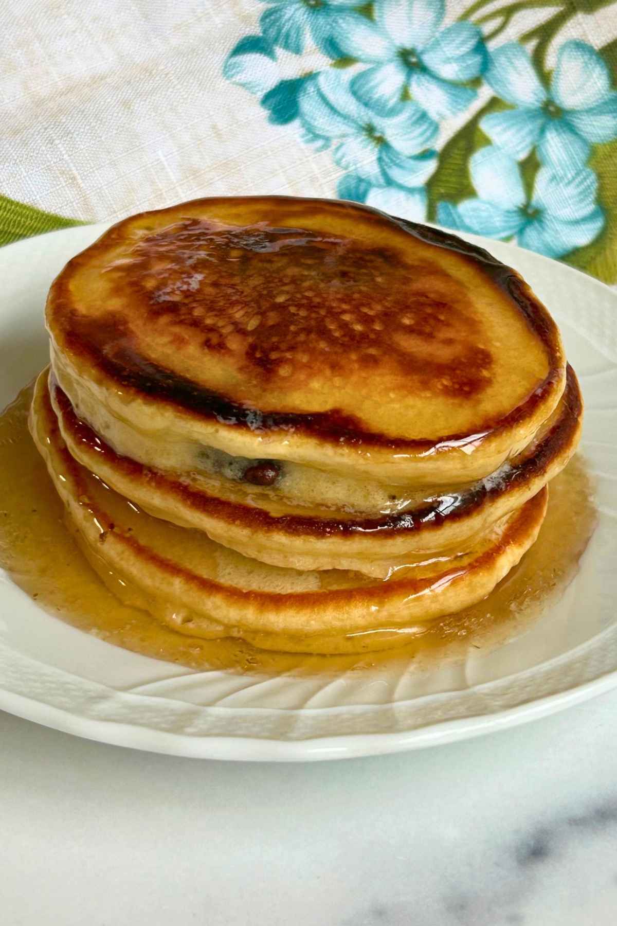 Close-up shot of stacked pancakes covered with butter and syrup on a white plate.