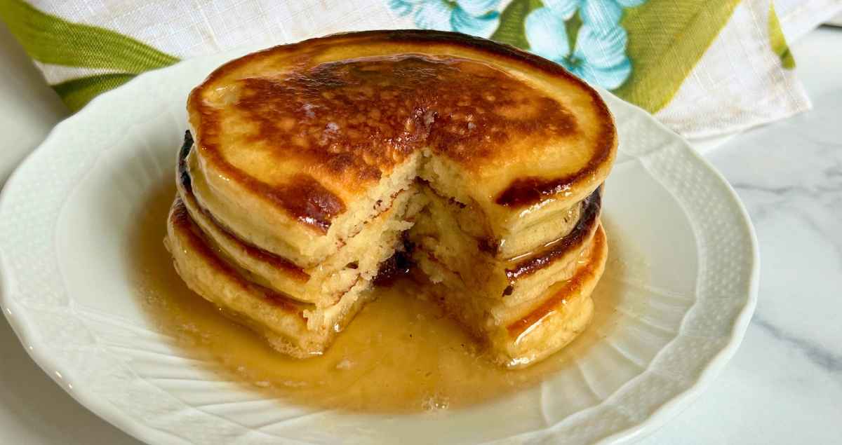 A stack of 3 pancakes topped with maple syrup and a portion cut out of the stack.